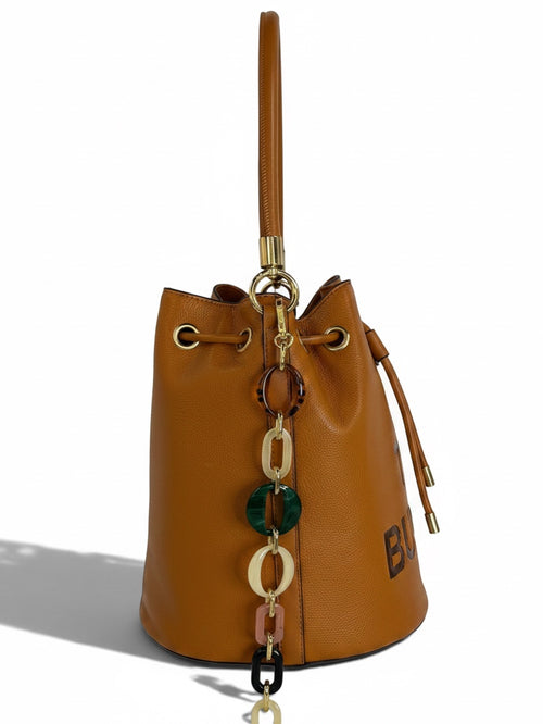 Zimoras Boutique tan pebbled vegan leather bucket bag with drawstring closure and decorative resin chain accents.