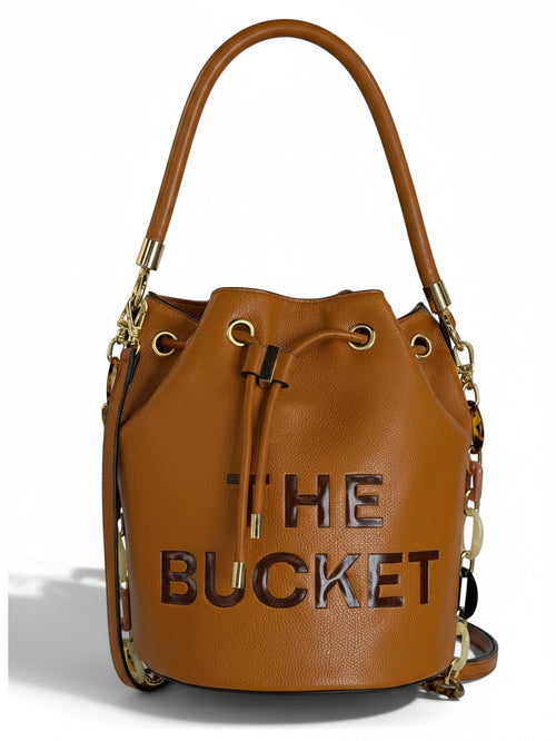 Zimoras Boutique tan pebbled vegan leather bucket bag with gold hardware, drawstring closure, and resin chain detail.